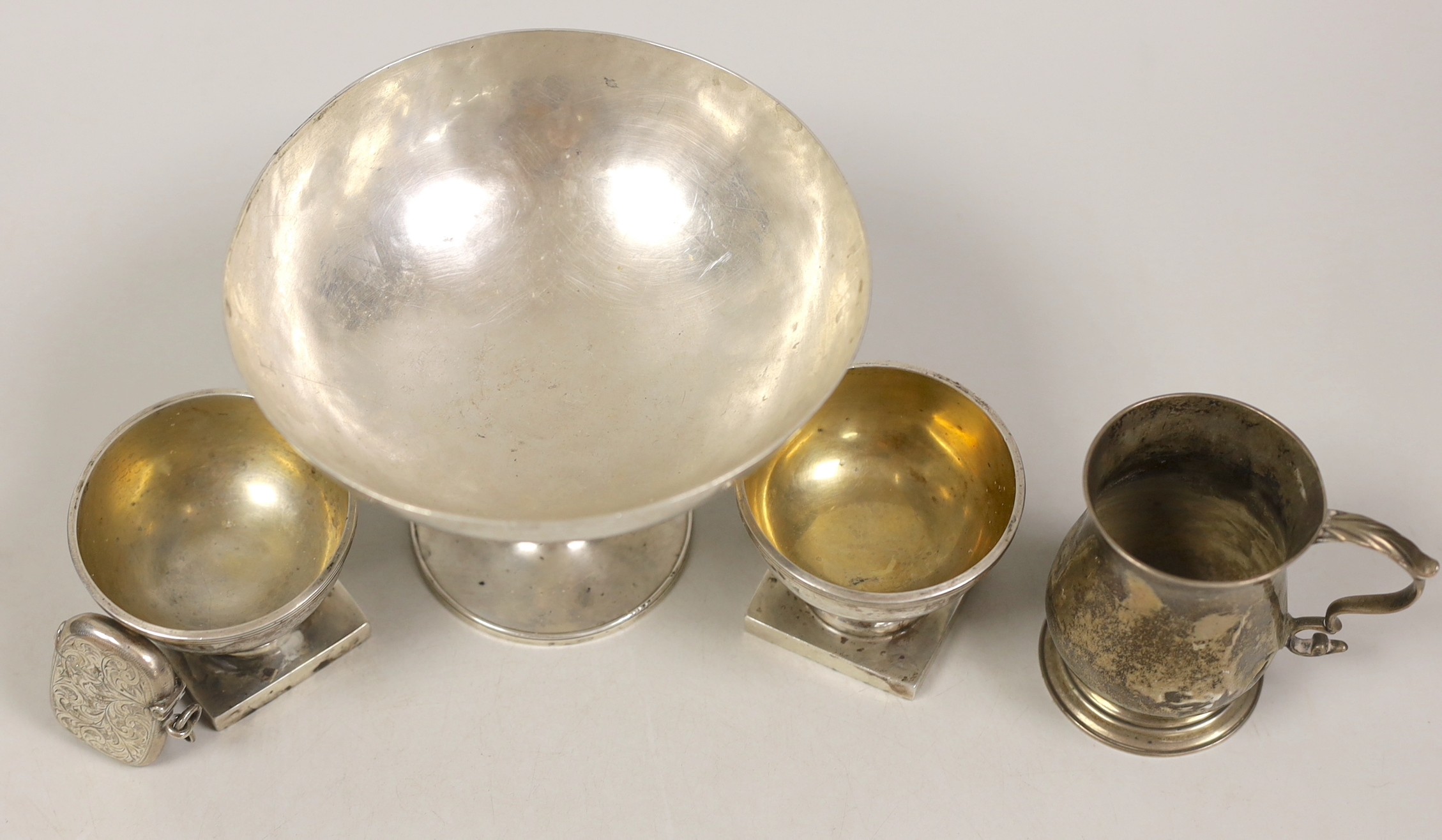 An Edwardian planished silver tazza, with engraved inscription, Robert Woodhouse, London, 1905, diameter 14cm, a small George III silver mug (a.f.), London, 1795, a pair of George V silver pedestal salts and a silver ves